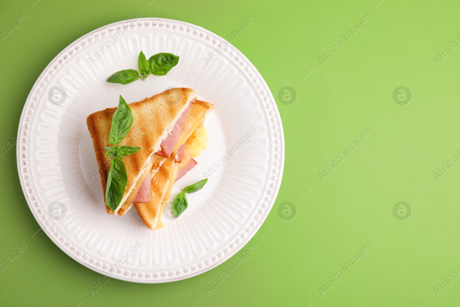 Photo of Pieces of toasted bread with melted cheese, ham and basil on green background, top view. Space for text