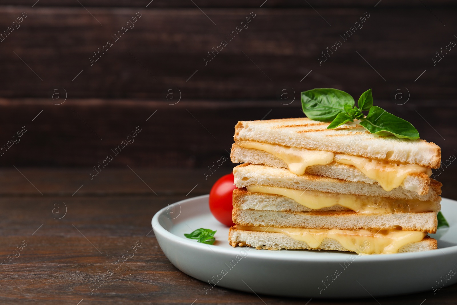 Photo of Pieces of toasted bread with melted cheese and basil on wooden table, space for text