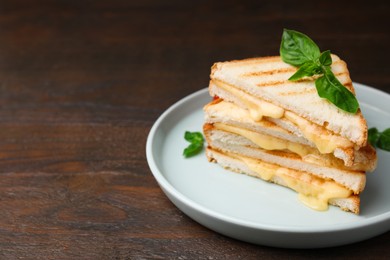 Pieces of toasted bread with melted cheese and basil on wooden table, space for text