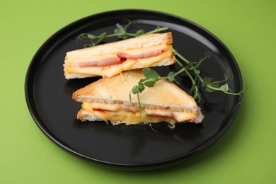 Photo of Pieces of toasted bread with melted cheese, ham and microgreens on green background