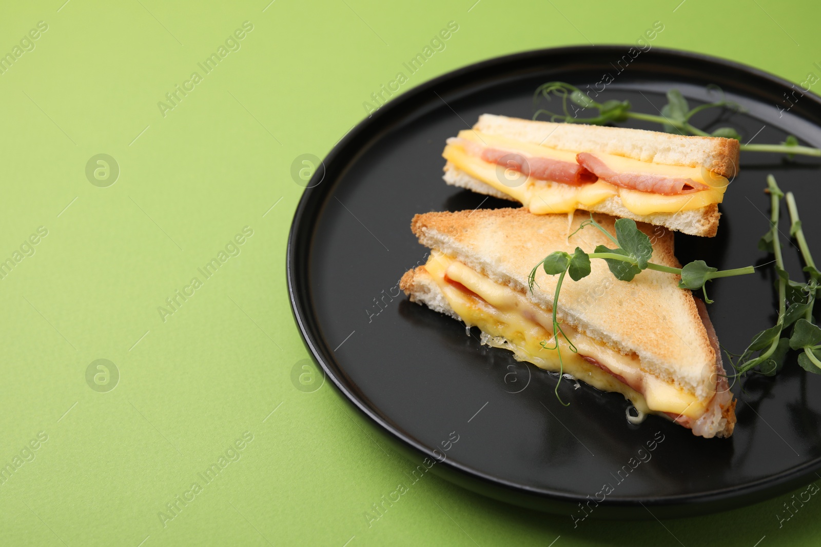 Photo of Pieces of toasted bread with melted cheese, ham and microgreens on green background, space for text