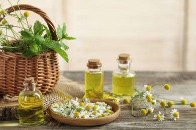 Photo of Beautiful chamomile flowers, bottles of essential oils and mint on wooden table