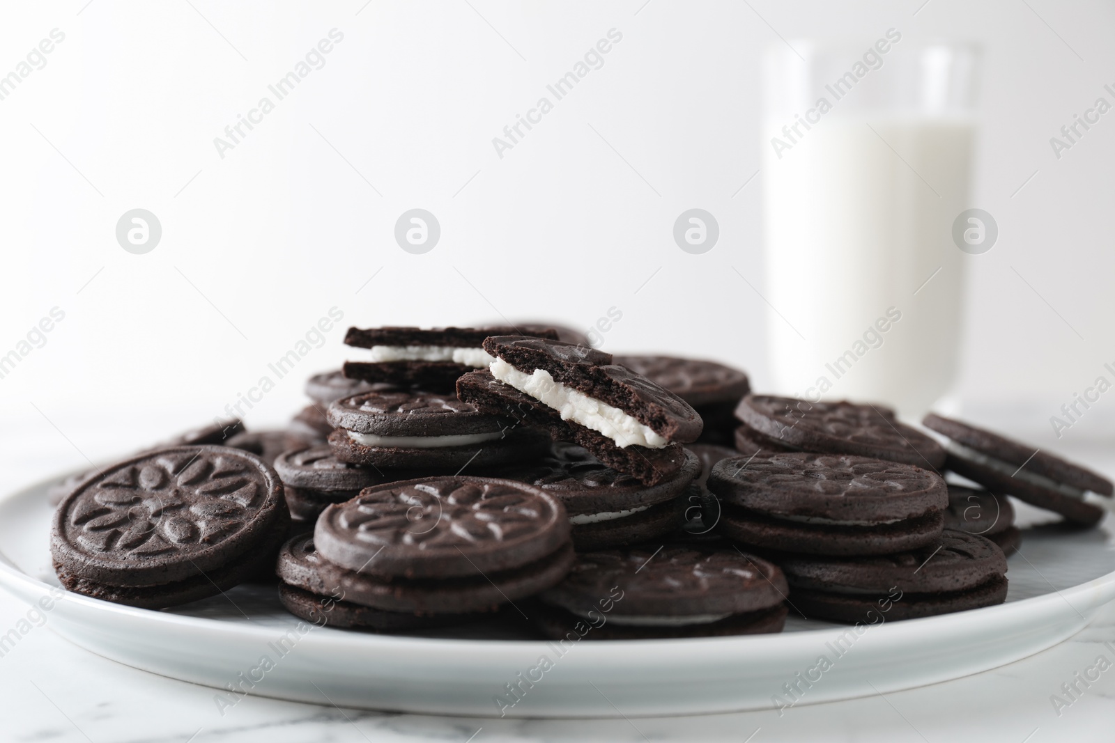 Photo of Tasty sandwich cookies and milk on white marble table