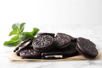 Tasty sandwich cookies and mint on white marble table