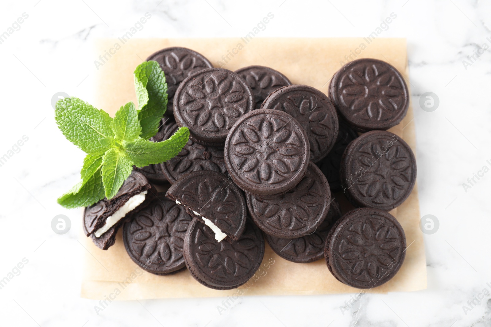 Photo of Tasty sandwich cookies and mint on white marble table, top view