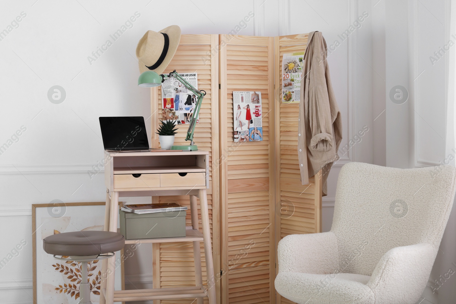 Photo of Folding screen, table, laptop, lamp and armchair indoors. Interior design