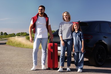 Photo of Happy family with red suitcase near car outdoors