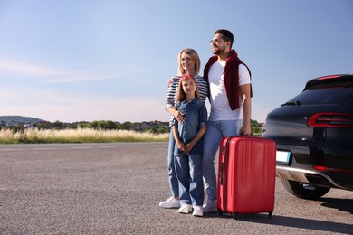 Photo of Happy family with red suitcase near car outdoors, space for text