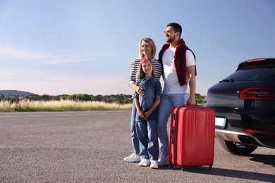 Happy family with red suitcase near car outdoors, space for text