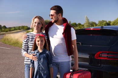 Photo of Happy family with red suitcase near car outdoors