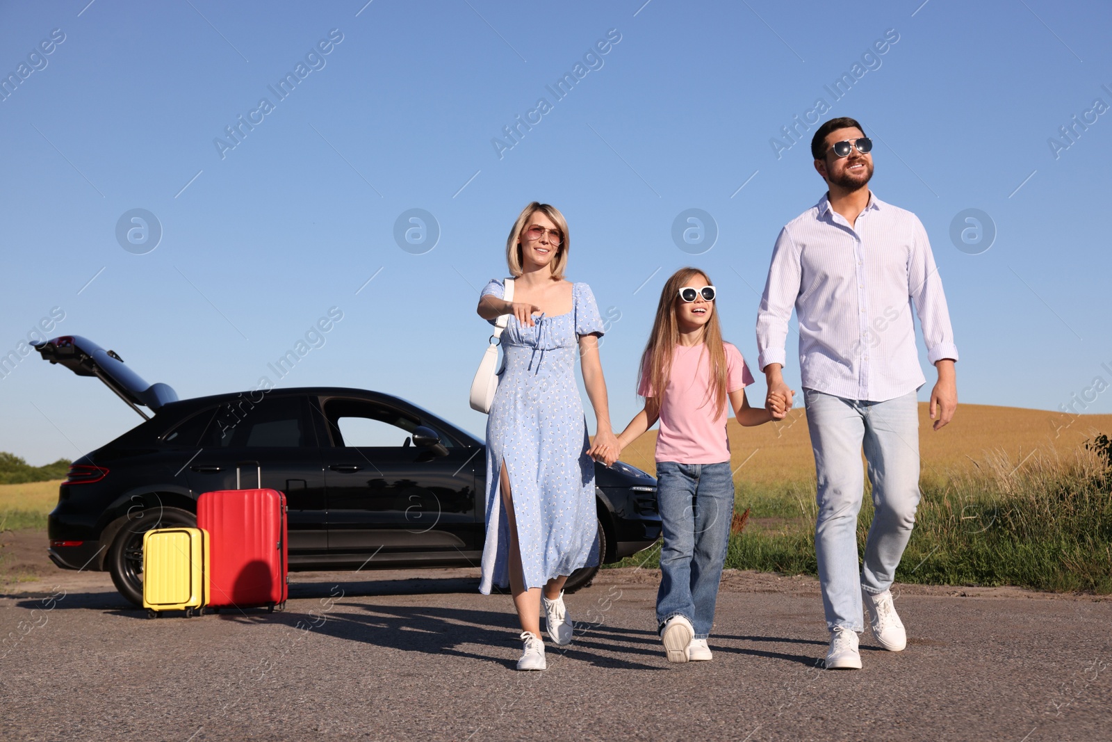 Photo of Parents, their daughter, car and suitcases outdoors. Family traveling