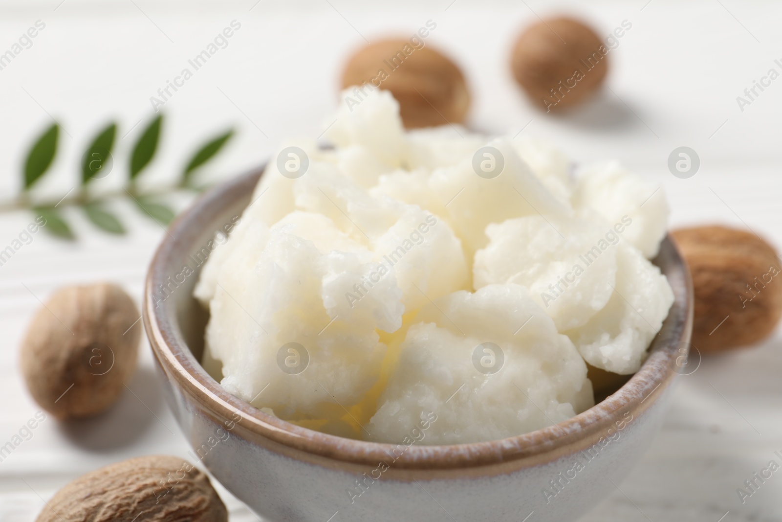 Photo of Shea butter in bowl and nuts on white wooden table, closeup