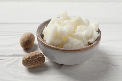 Shea butter in bowl and nuts on white wooden table, closeup