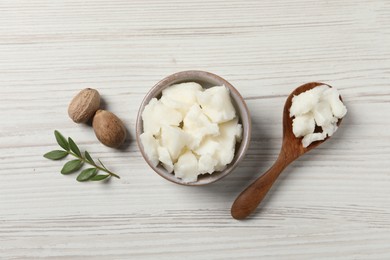 Shea butter in bowl, spoon and nuts on white wooden table, flat lay