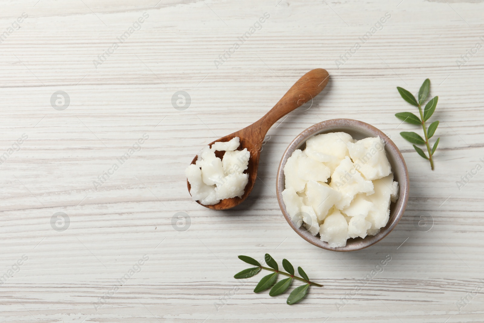 Photo of Shea butter in bowl and spoon on white wooden table, flat lay. Space for text