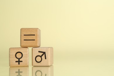 Photo of Gender equality concept. Wooden cubes with male and female symbols on light yellow background, space for text