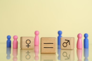 Photo of Gender equality concept. Wooden cubes with male and female figures on light yellow background, selective focus