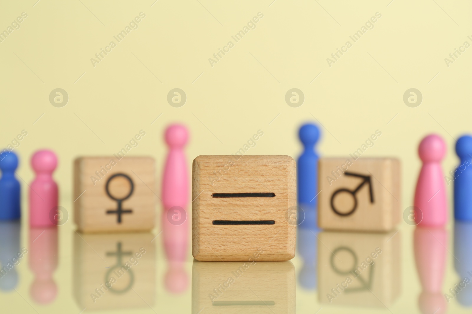 Photo of Gender equality concept. Wooden cubes with male and female figures on light yellow background, selective focus