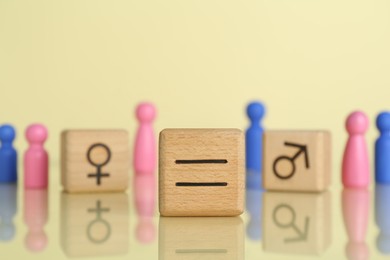 Gender equality concept. Wooden cubes with male and female figures on light yellow background, selective focus