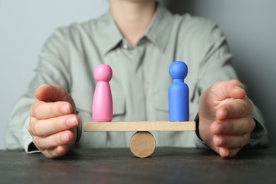 Gender equality concept. Woman with male and female figures on scales at dark table, closeup