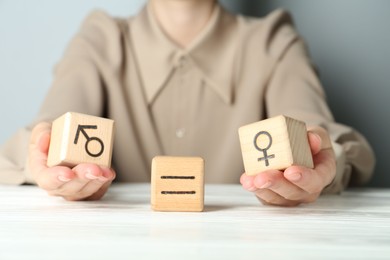 Gender equality concept. Woman with wooden cubes of male and female symbols at white table, closeup