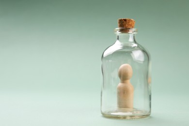 Loneliness concept. Human figure in bottle on light green background. Space for text