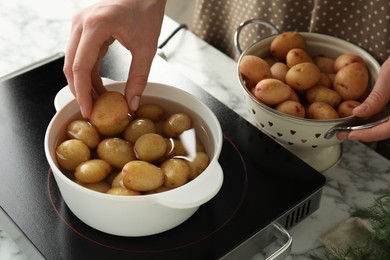 Woman putting potato into metal pot on stove, closeup