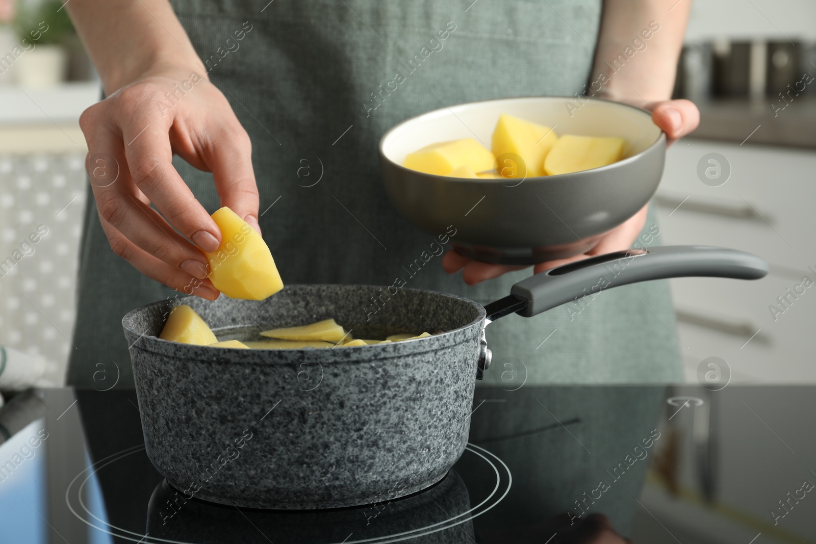 Photo of Woman putting potato into saucepan on stove, closeup