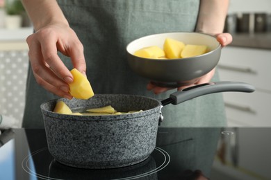 Photo of Woman putting potato into saucepan on stove, closeup