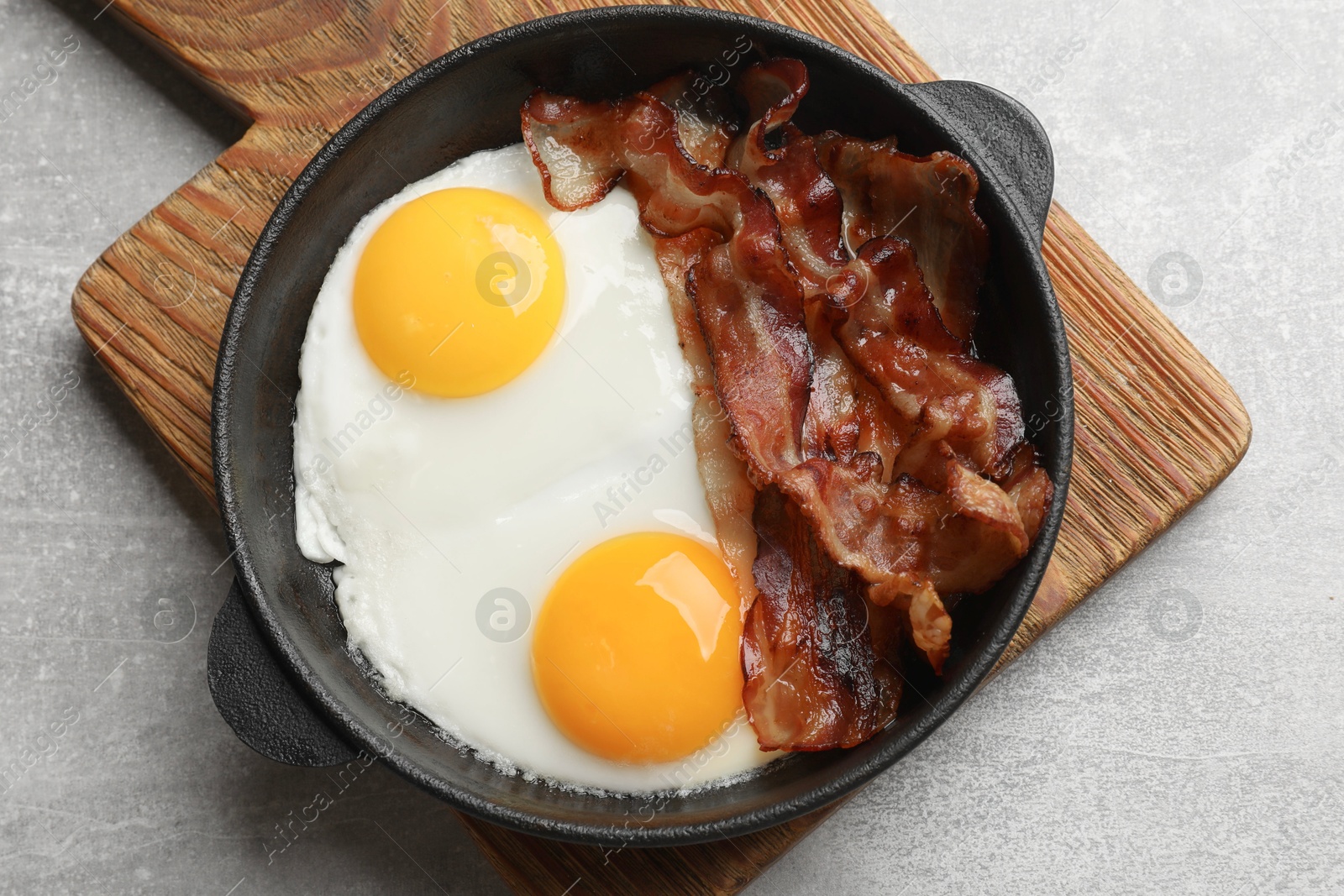 Photo of Tasty bacon and eggs in dish on gray textured table, top view