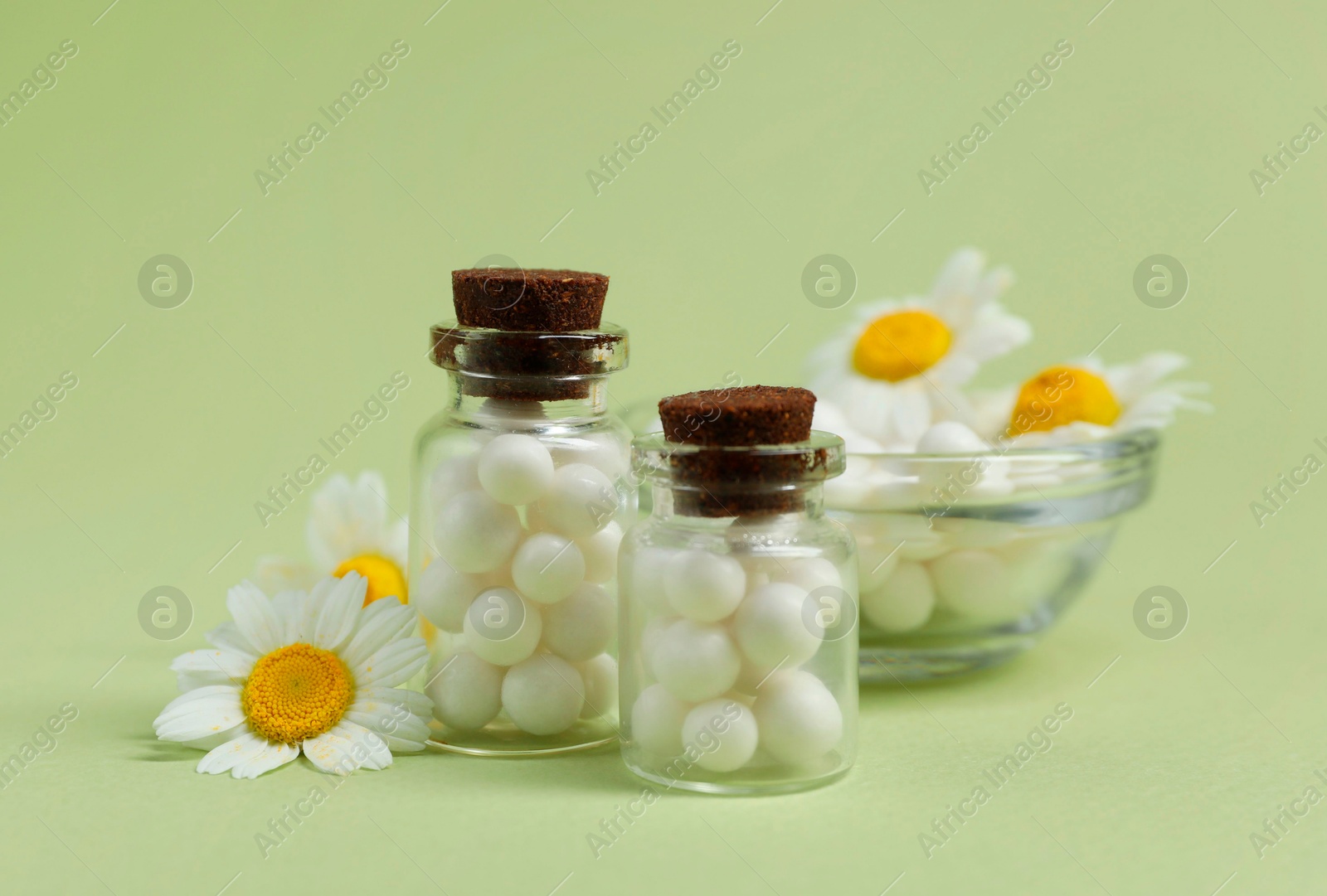 Photo of Homeopathic remedy and chamomiles on light green background, closeup