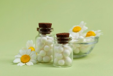 Homeopathic remedy and chamomiles on light green background, closeup