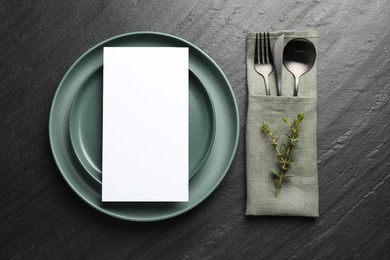 Photo of Empty menu, plates, cutlery, napkin and floral decor on black table, top view. Mockup for design