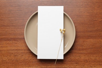 Empty menu, plate and dry flowers on wooden table, top view. Mockup for design