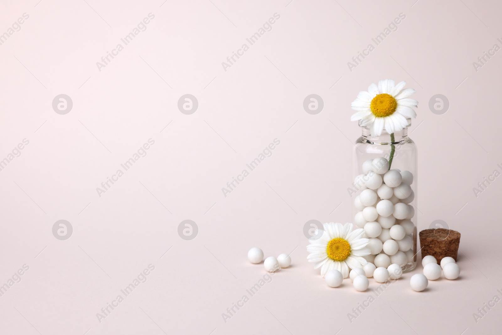 Photo of Homeopathy. Glass bottle, pills and chamomiles on beige background, space for text