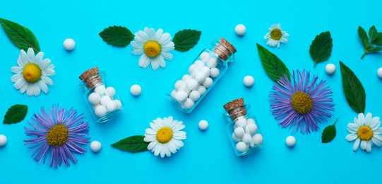 Homeopathy. Glass bottles, pills, flowers and green leaves on light blue background, flat lay