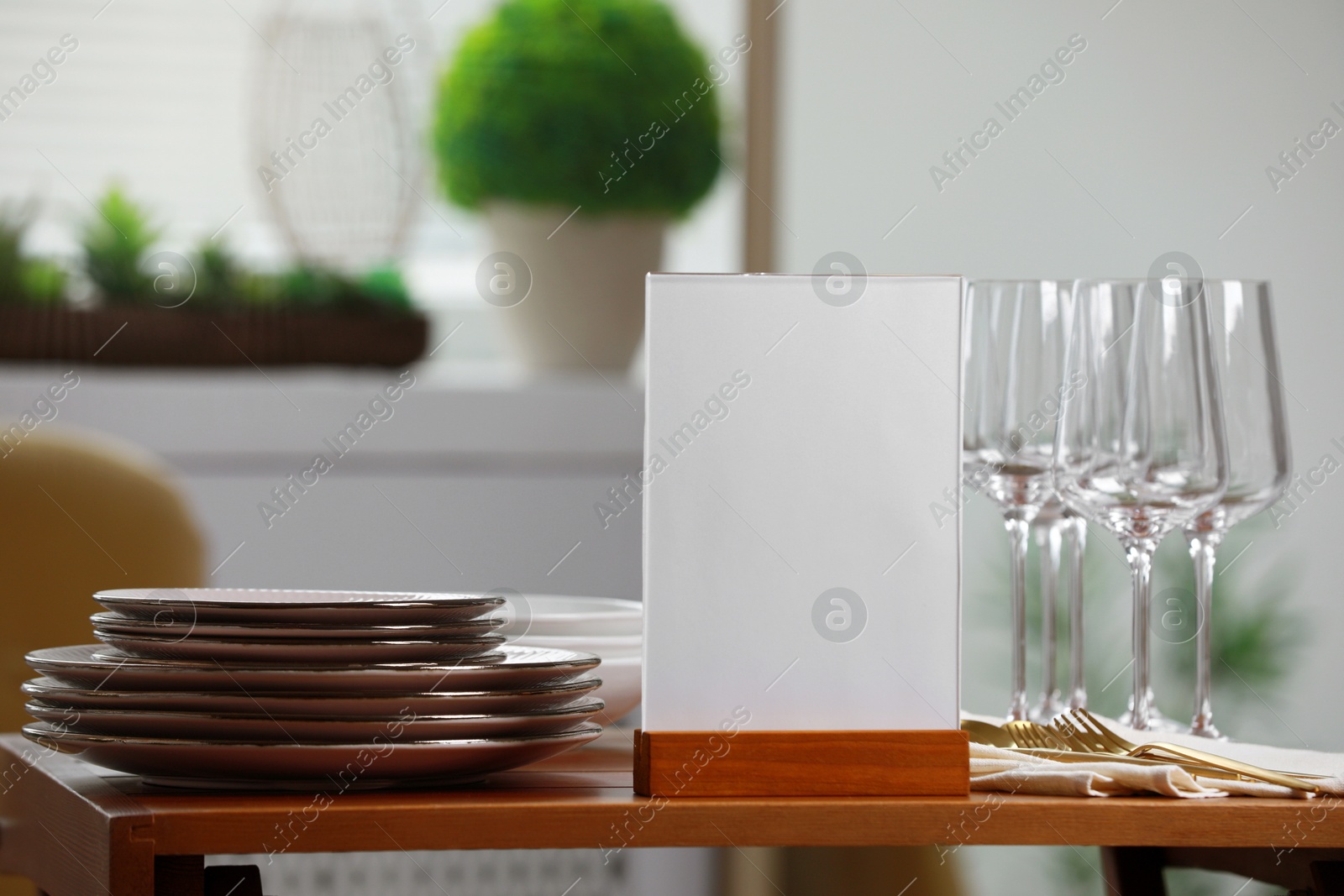 Photo of Menu holder, clean dishware and cutlery on wooden table indoors