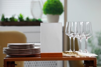 Photo of Menu holder, clean dishware and cutlery on wooden table indoors