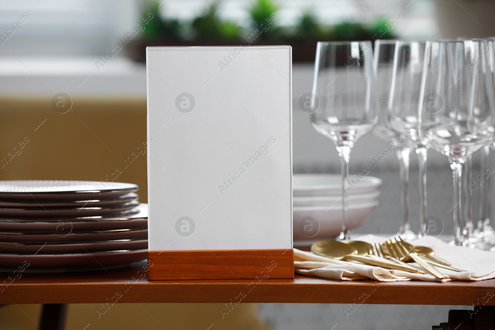 Photo of Menu holder, clean dishware and cutlery on wooden table indoors