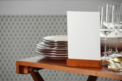 Photo of Menu holder, clean dishware and cutlery on wooden table indoors