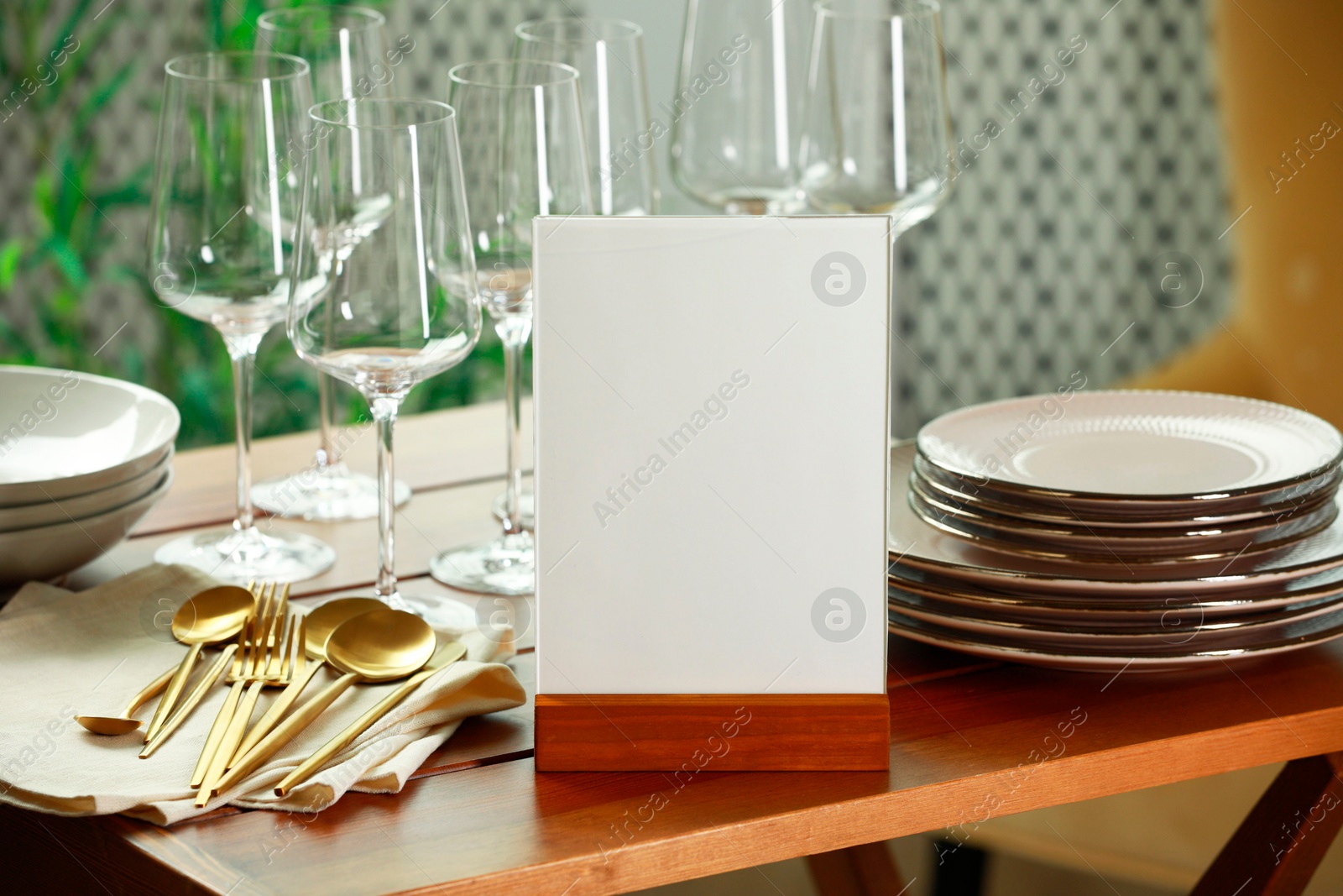 Photo of Menu holder, clean dishware and cutlery on wooden table indoors