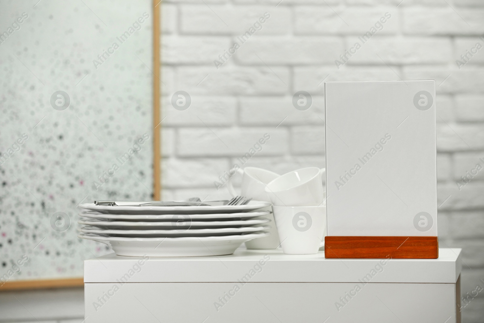 Photo of Menu holder and clean dishware on white table indoors