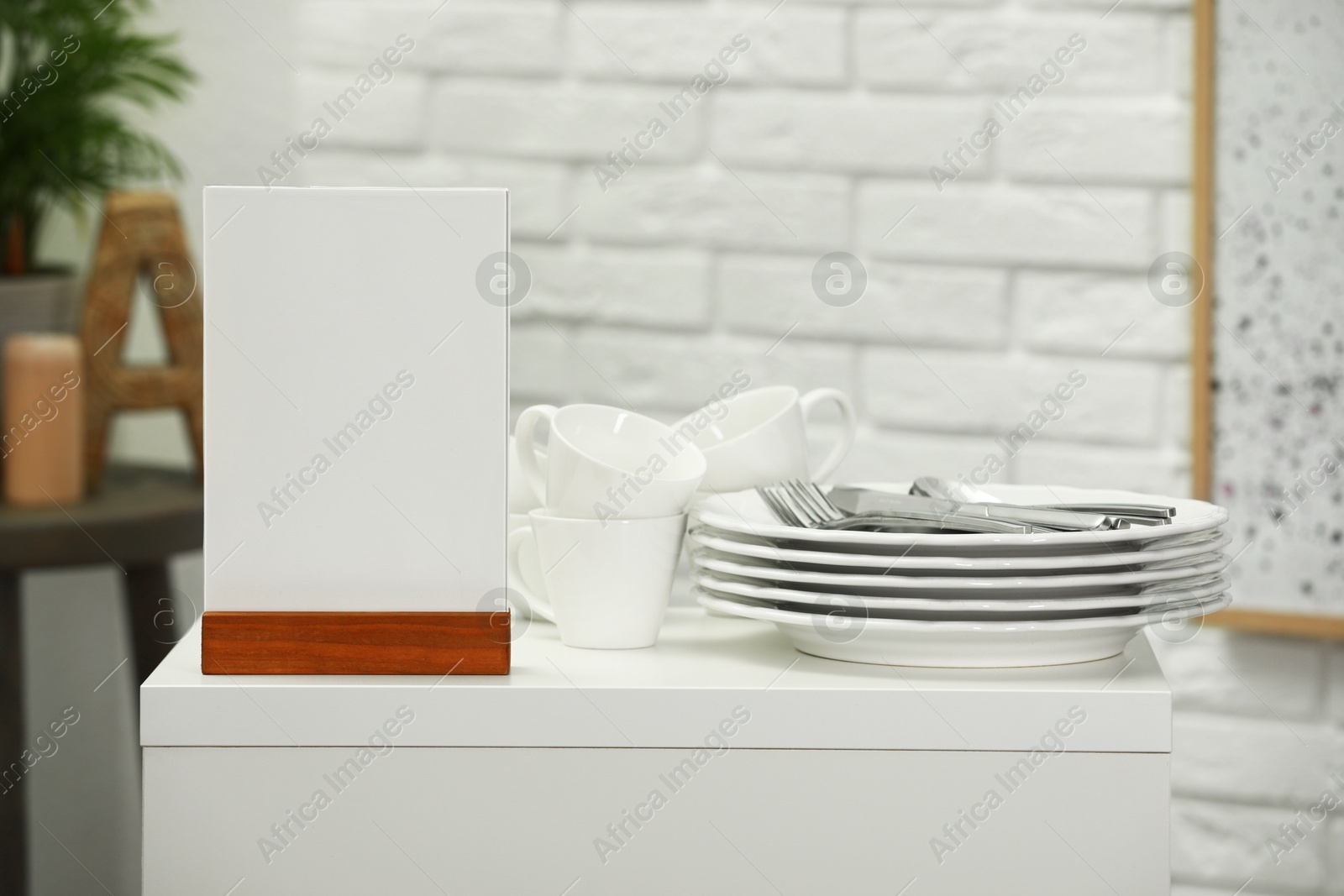 Photo of Menu holder and clean dishware on white table indoors