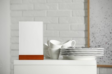 Photo of Menu holder and clean dishware on white table indoors