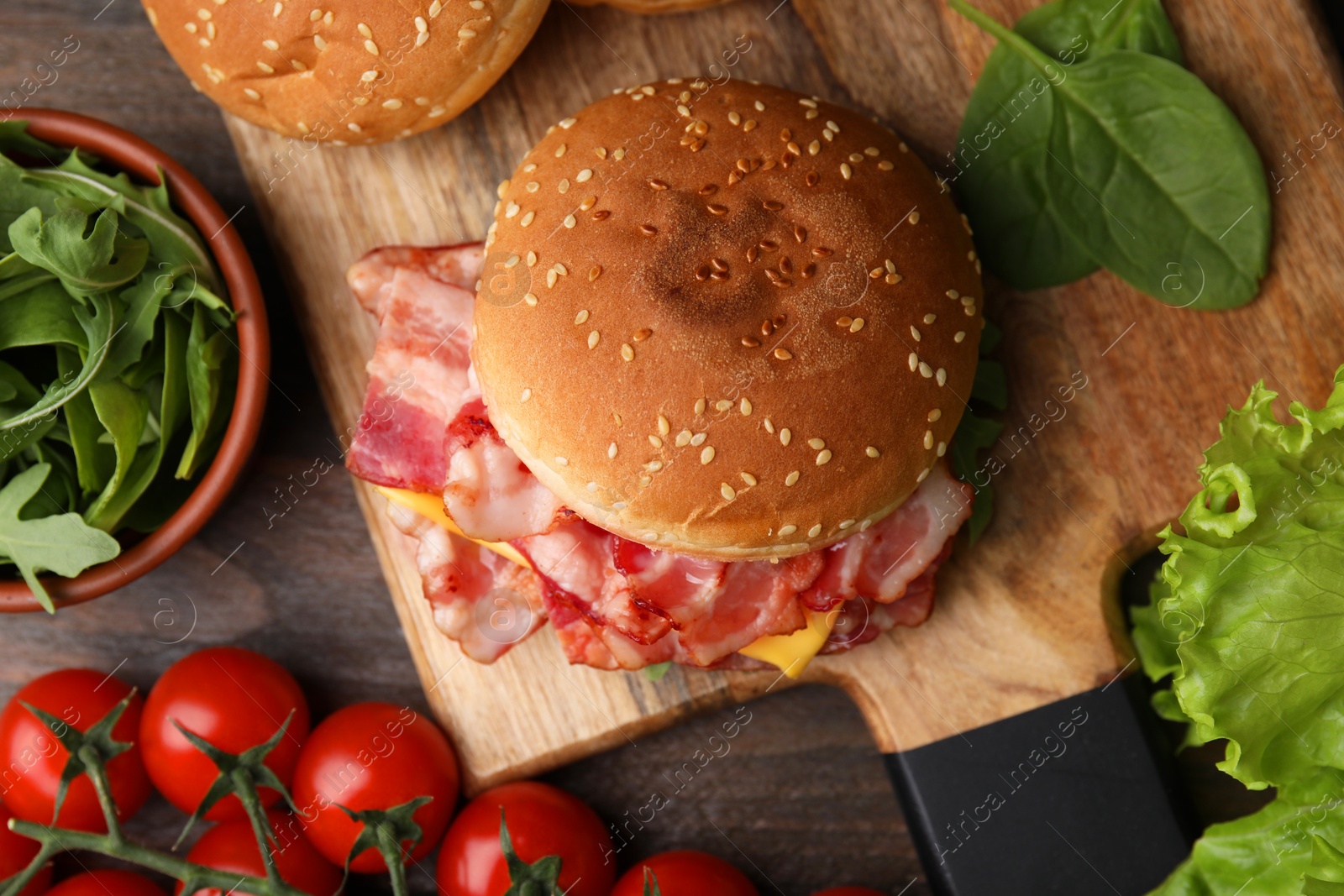 Photo of Delicious burger with bacon, cheese, tomatoes and greens on wooden table, top view