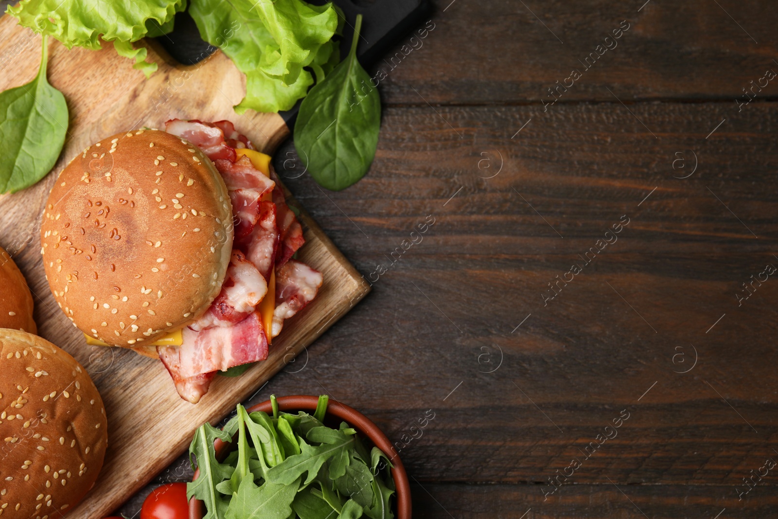 Photo of Delicious burger with bacon, cheese and greens on wooden table, top view. Space for text