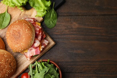 Photo of Delicious burger with bacon, cheese and greens on wooden table, top view. Space for text