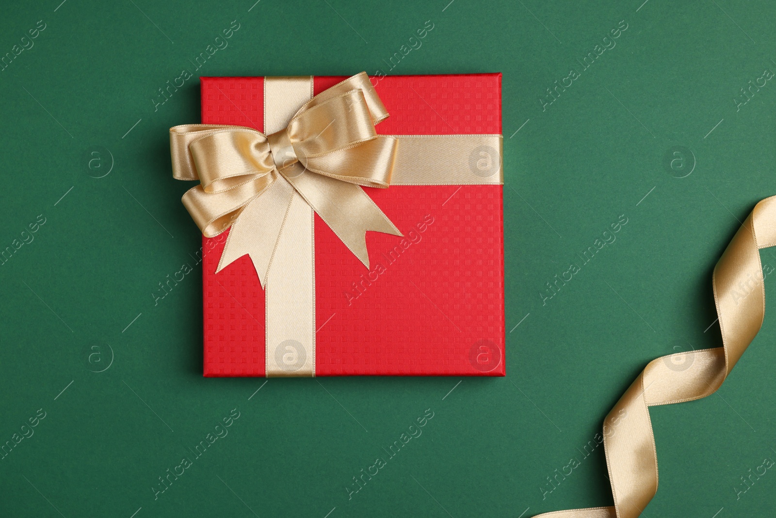 Photo of Beautiful red gift box with bow and ribbons on green background, flat lay