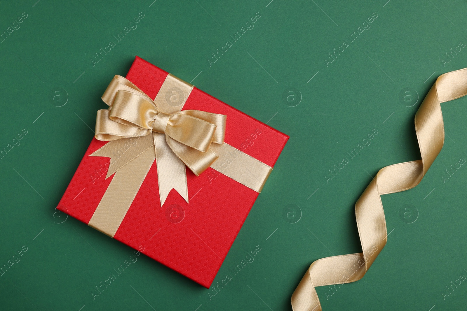 Photo of Beautiful red gift box with bow and ribbons on green background, flat lay