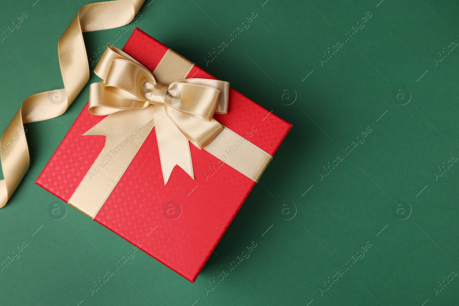 Photo of Beautiful red gift box with bow and ribbons on green background, flat lay. Space for text